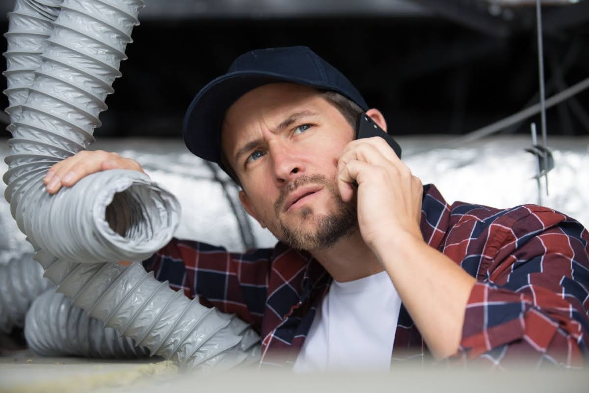 Confused man on the phone with a technician as he holds HVAC ductwork in his other hand