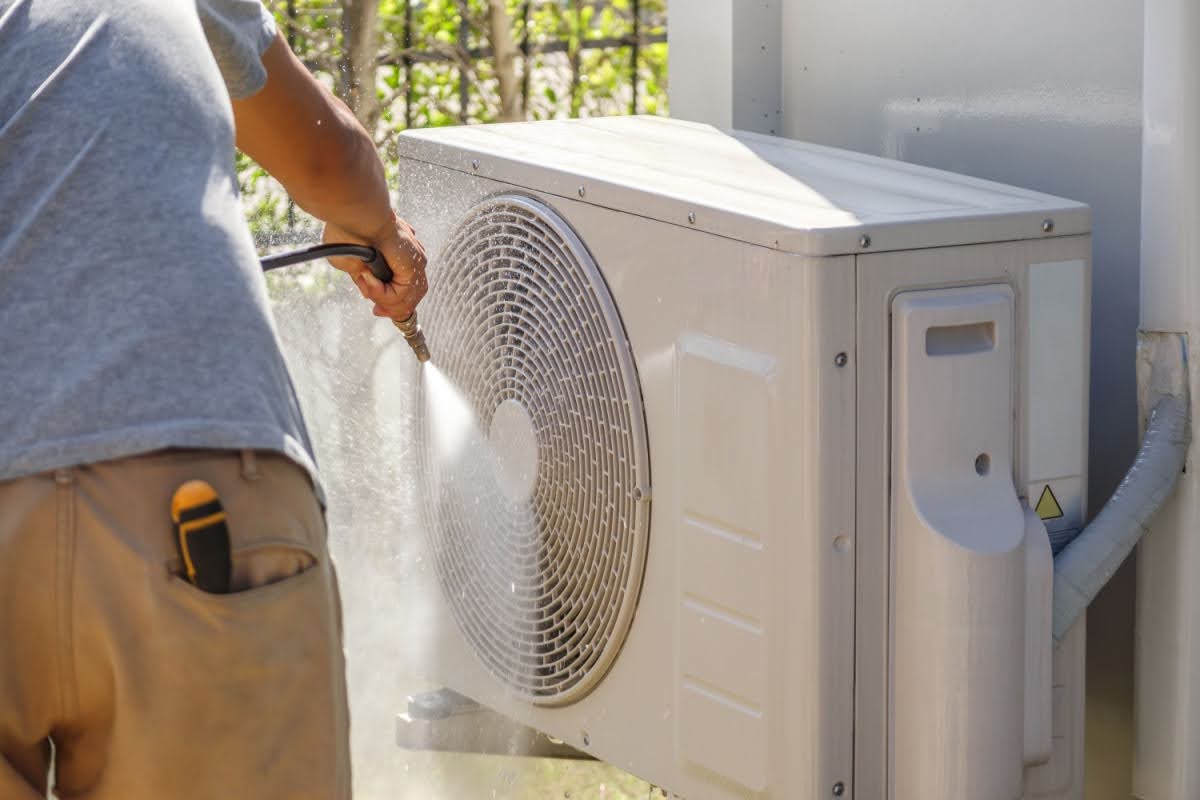 HVAC technician spraying down an outdoor AC unit to prepare it for the summer season