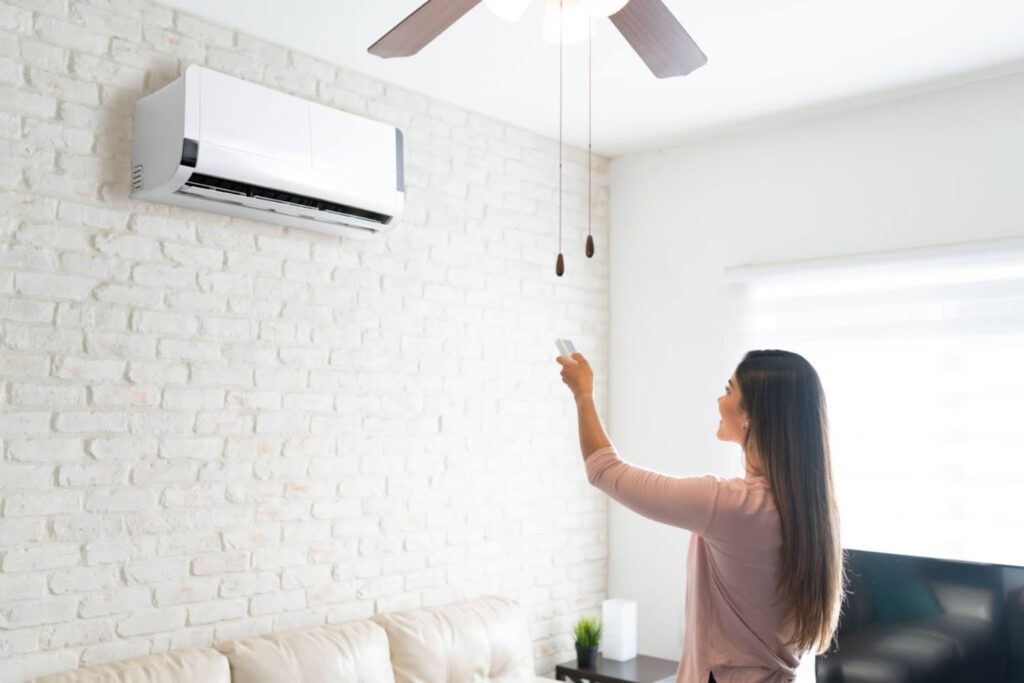 Woman standing in front of ductless AC mini split unit as she turns it on with a remote