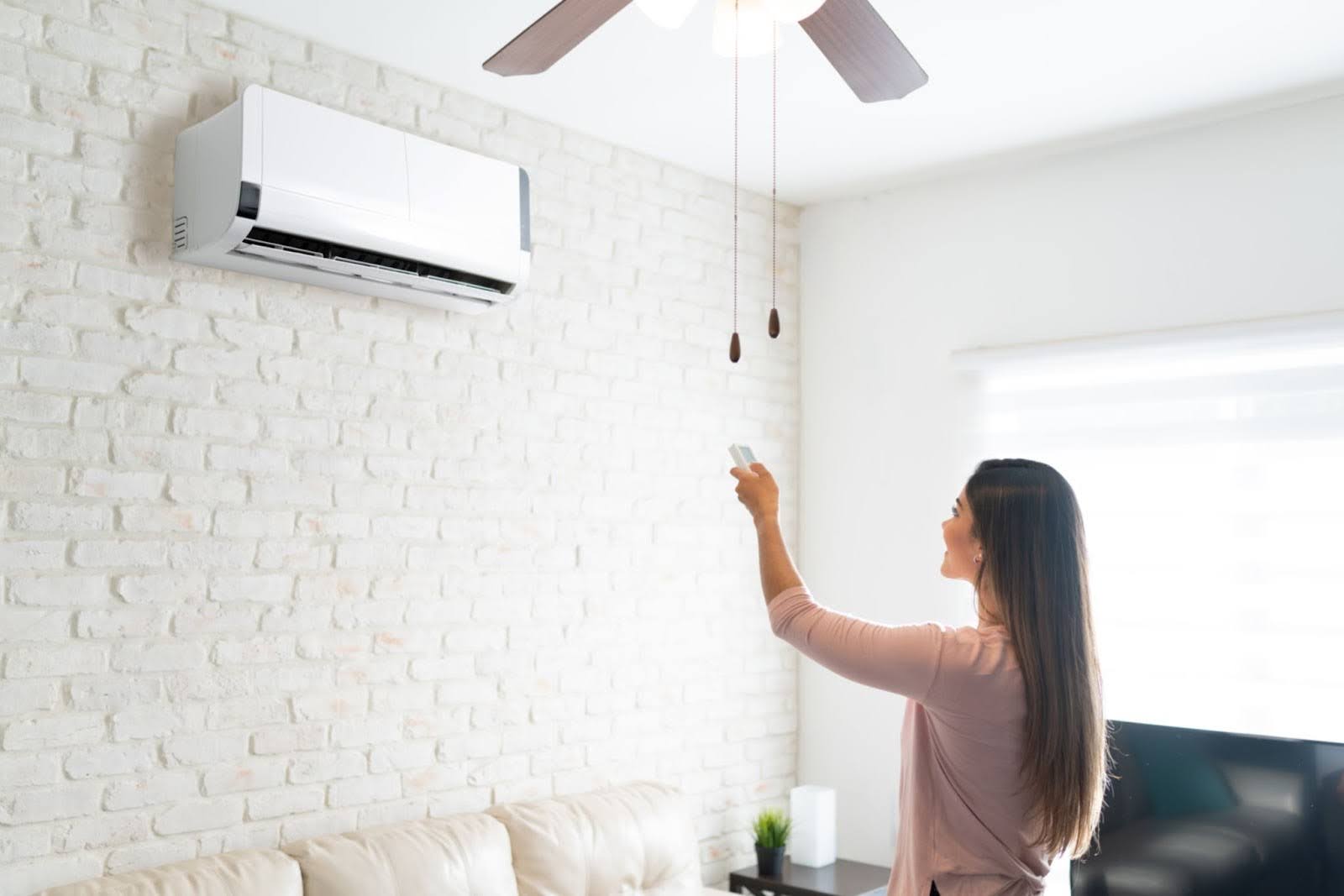 Woman standing in front of ductless AC mini split unit as she turns it on with a remote