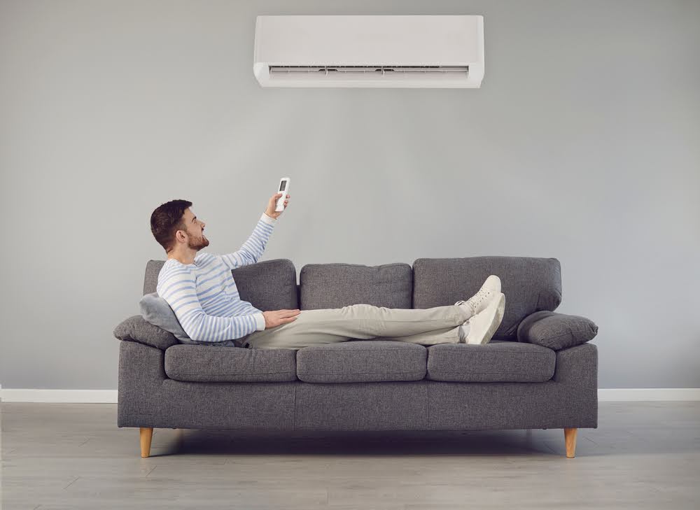 The young man turns on the air conditioner while sitting on the sofa