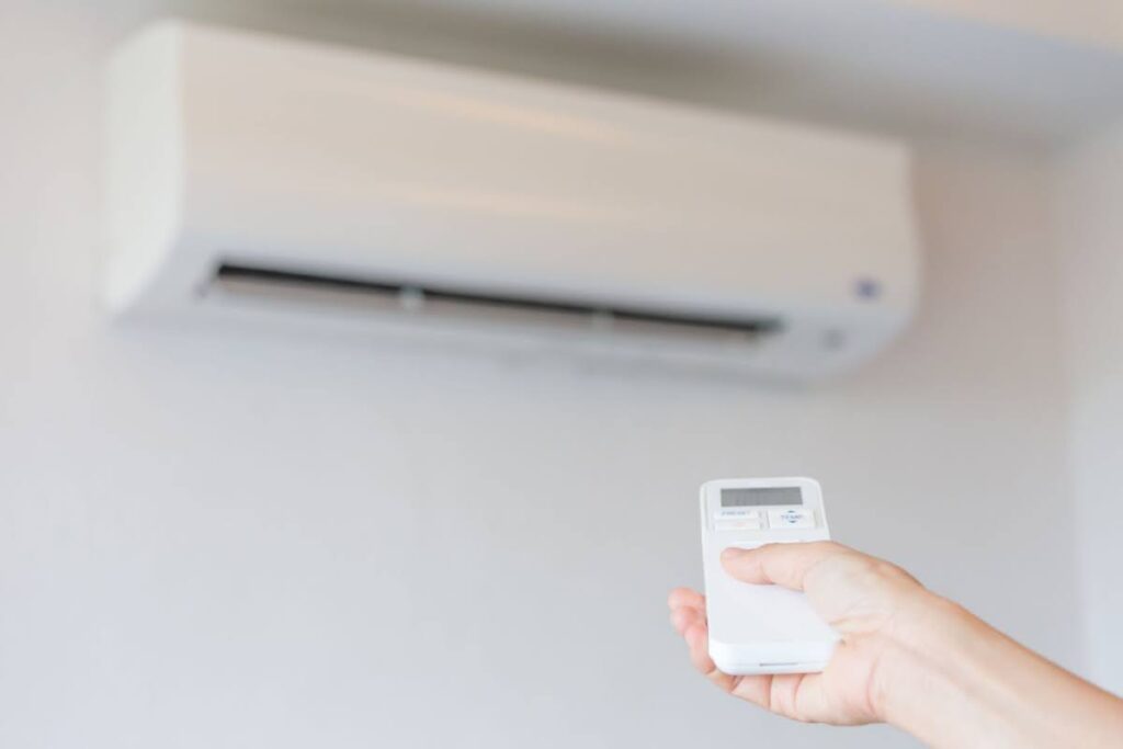 a hand holding a remote control to a ductless mini split unit - the unit is in the background and not turning on