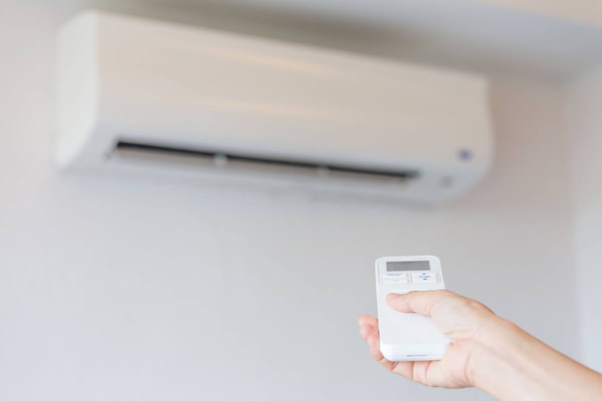 a hand holding a remote control to a ductless mini split unit - the unit is in the background and not turning on