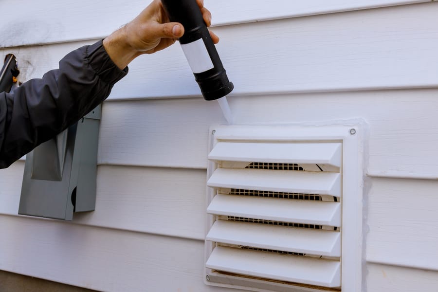 hand air sealing a vent on exterior of home